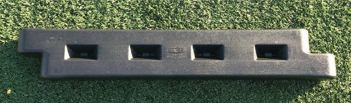 Black plastic playground border with four rectangular slots, installed on green artificial turf, featuring a spike for secure placement.