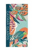 A rectangular beach towel featuring a vibrant tropical print of a parrot, papayas, and coral, with a dark teal vertical band on the left side printed with the text 'CAYMAN ISLANDS' in white.