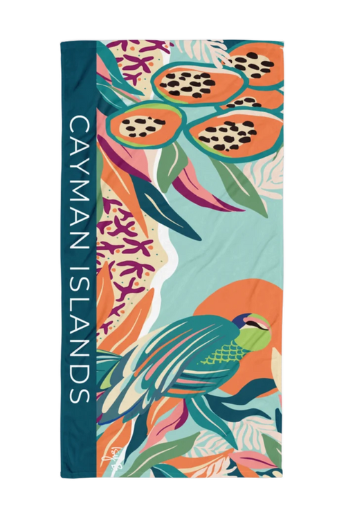 A rectangular beach towel featuring a vibrant tropical print of a parrot, papayas, and coral, with a dark teal vertical band on the left side printed with the text 'CAYMAN ISLANDS' in white.