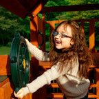 Child playing with green heavy-duty plastic ship's wheel attached to wooden swing set accessory