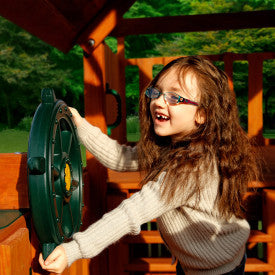 Child playing with green heavy-duty plastic ship's wheel attached to wooden swing set accessory