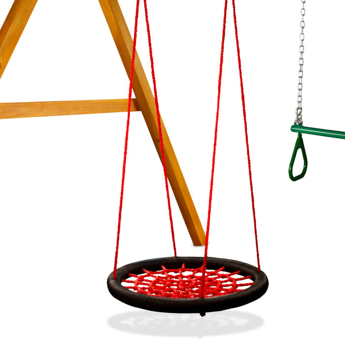 Red woven round swing with black heavy-duty ring hanging from wooden swing set frame, next to green trapeze bar
