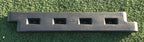 Black plastic playground border with four rectangular slots, installed on green artificial turf, featuring a spike for secure placement.