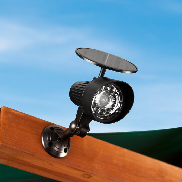 Black solar-powered LED spotlight with circular bulbs mounted on wooden playset beam against blue sky