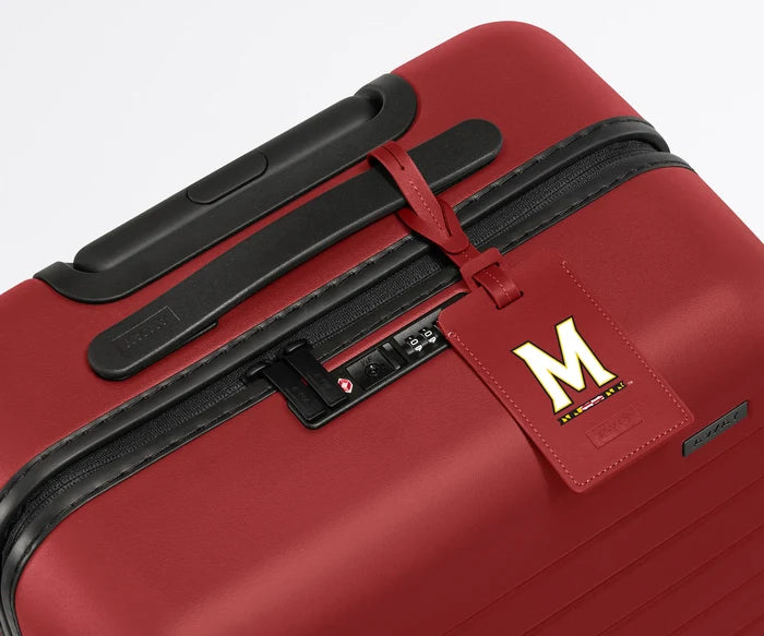 Red luggage tag with the University of Maryland logo on it attached to a red hardside suitcase.